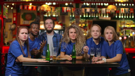 Emotional-fans-in-blue-shirts-at-a-beer-bar.-A-multi-ethnic-group-of-African-American-people-are-upset-and-sad-because-of-the-failure-of-their-team.-Defeat-of-your-favorite-football-volleyball-basketball-hockey-team.
